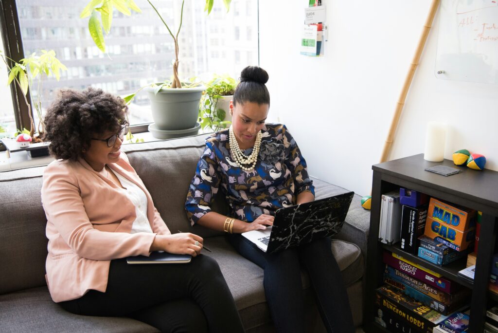 Two female adults sitting on a sofa looking at a laptop screen on one females lap